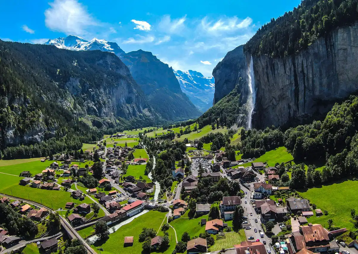 Houses on green grass field near mountain under blue sky during daytime — Lauterbrunnen, Switzerland