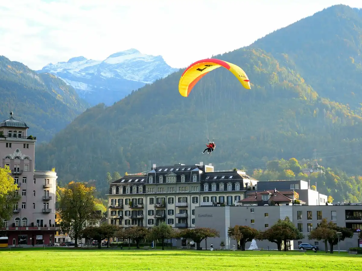 A paraglider is flying over a city with mountains in the background — Interlaken, Switzerland
