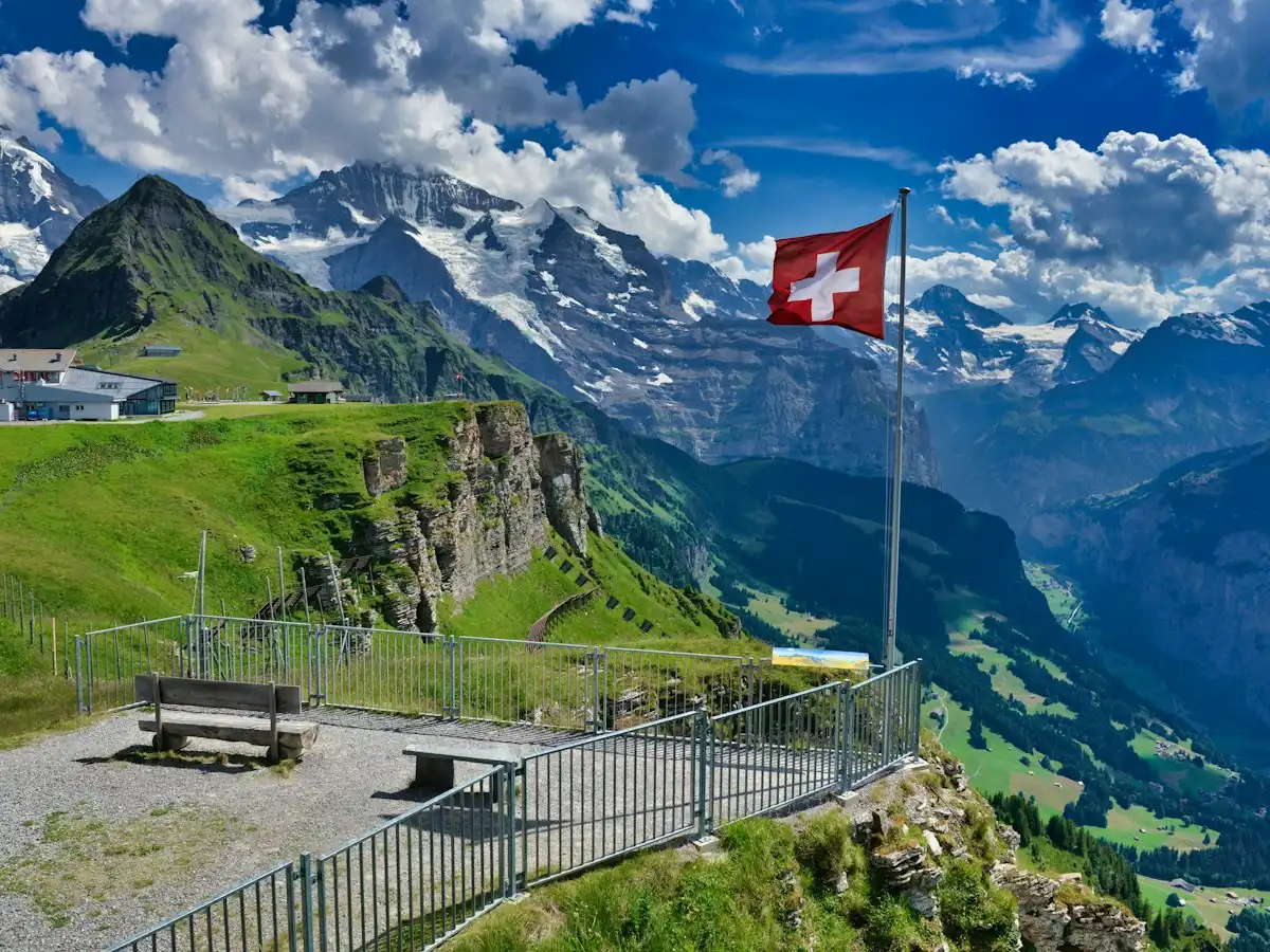 A flag on a pole in front of a mountain range — Swiss flag, Switzerland