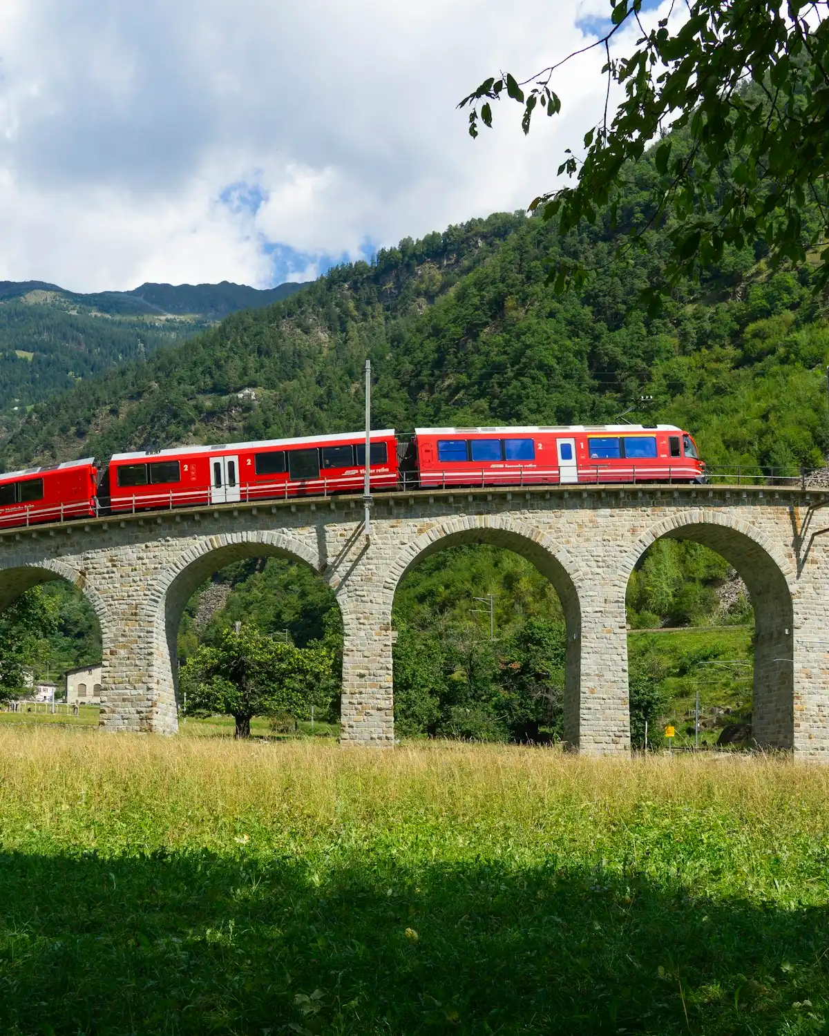 Red train crosses a stone viaduct in the mountains — Brusio, Bernina line, Switzerland